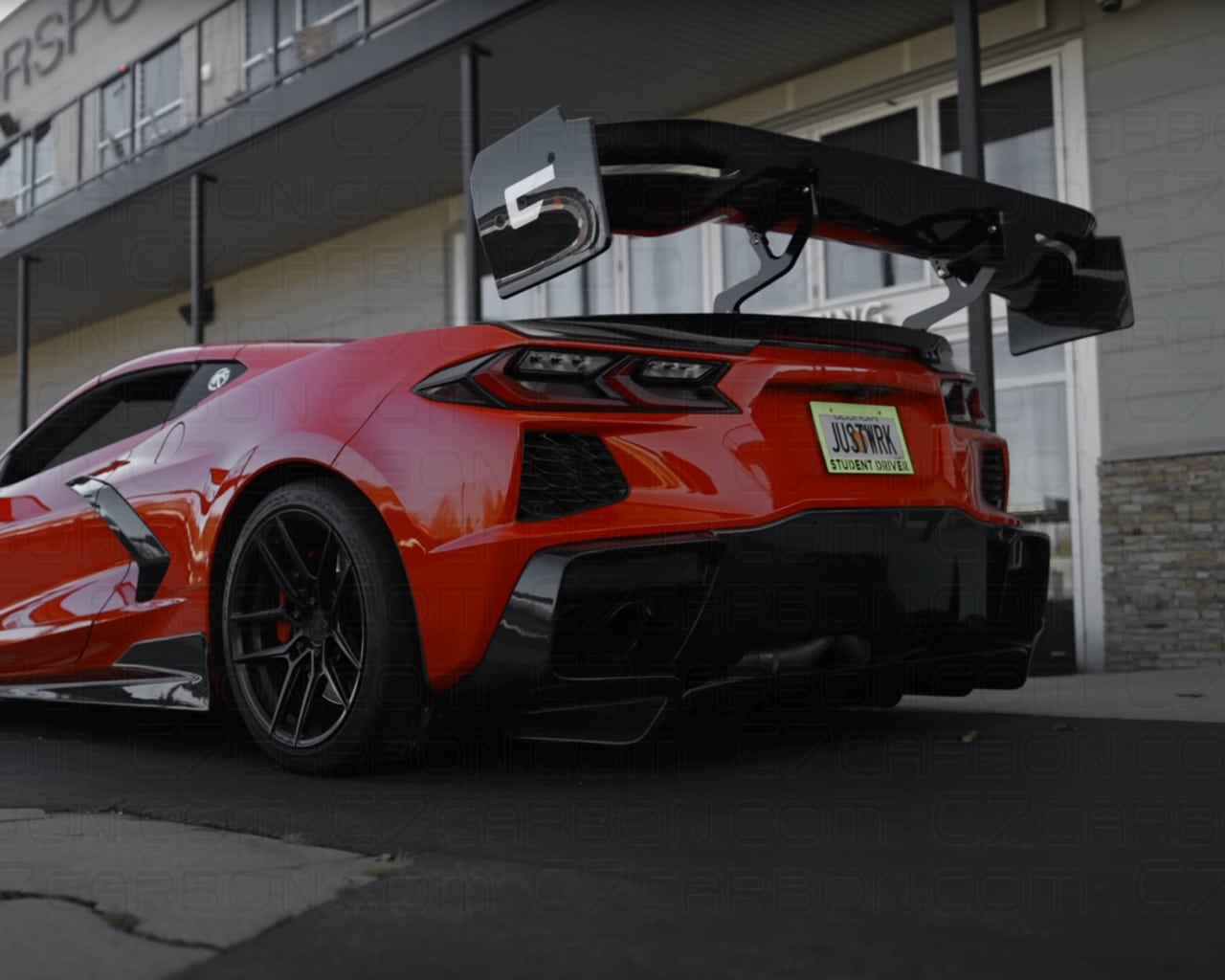 Red Corvette C8 driving on a track with a mounted rear spoiler.